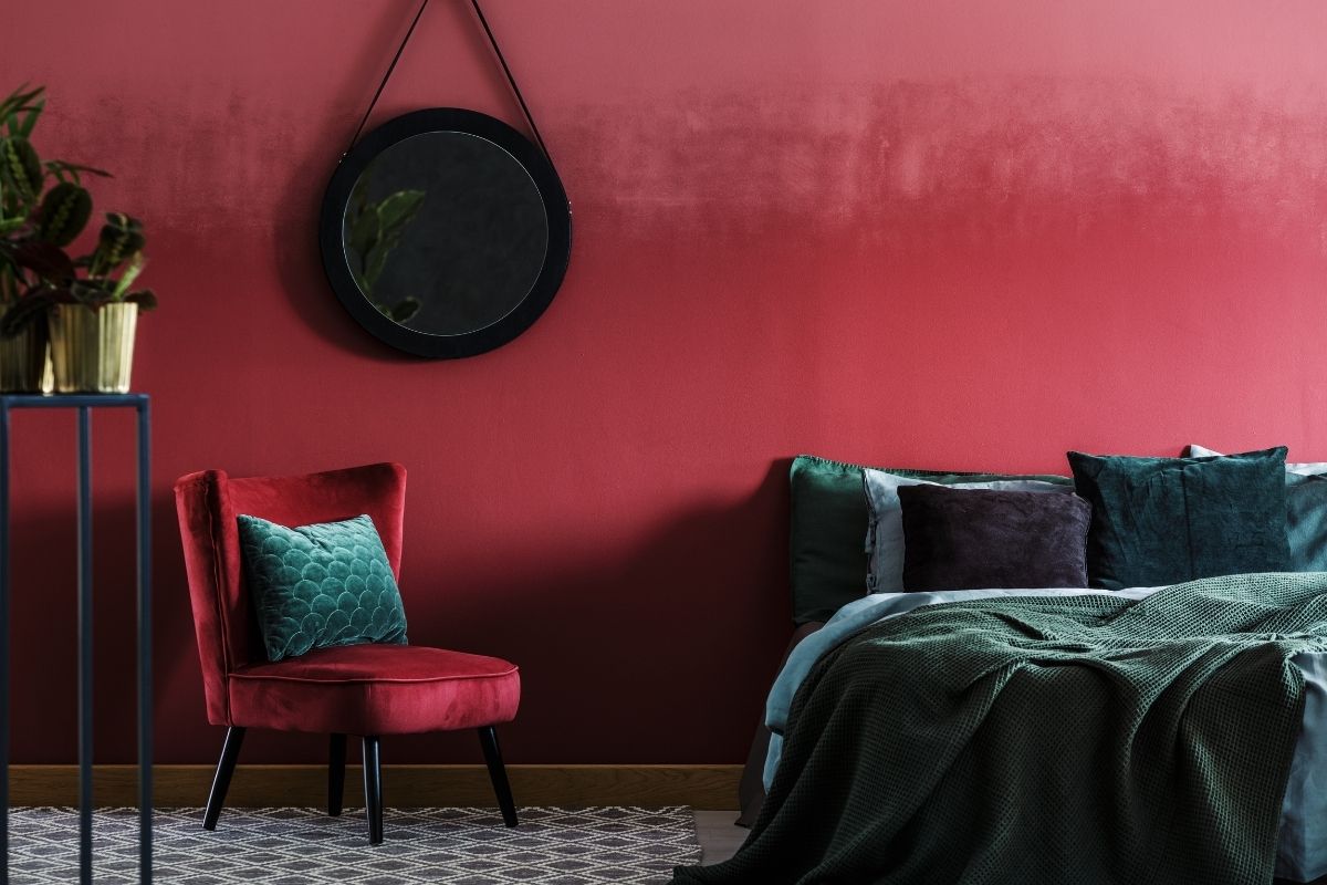 Camera con pareti borgogna, poltroncina in velluto rosso e biancheria verde petrolio