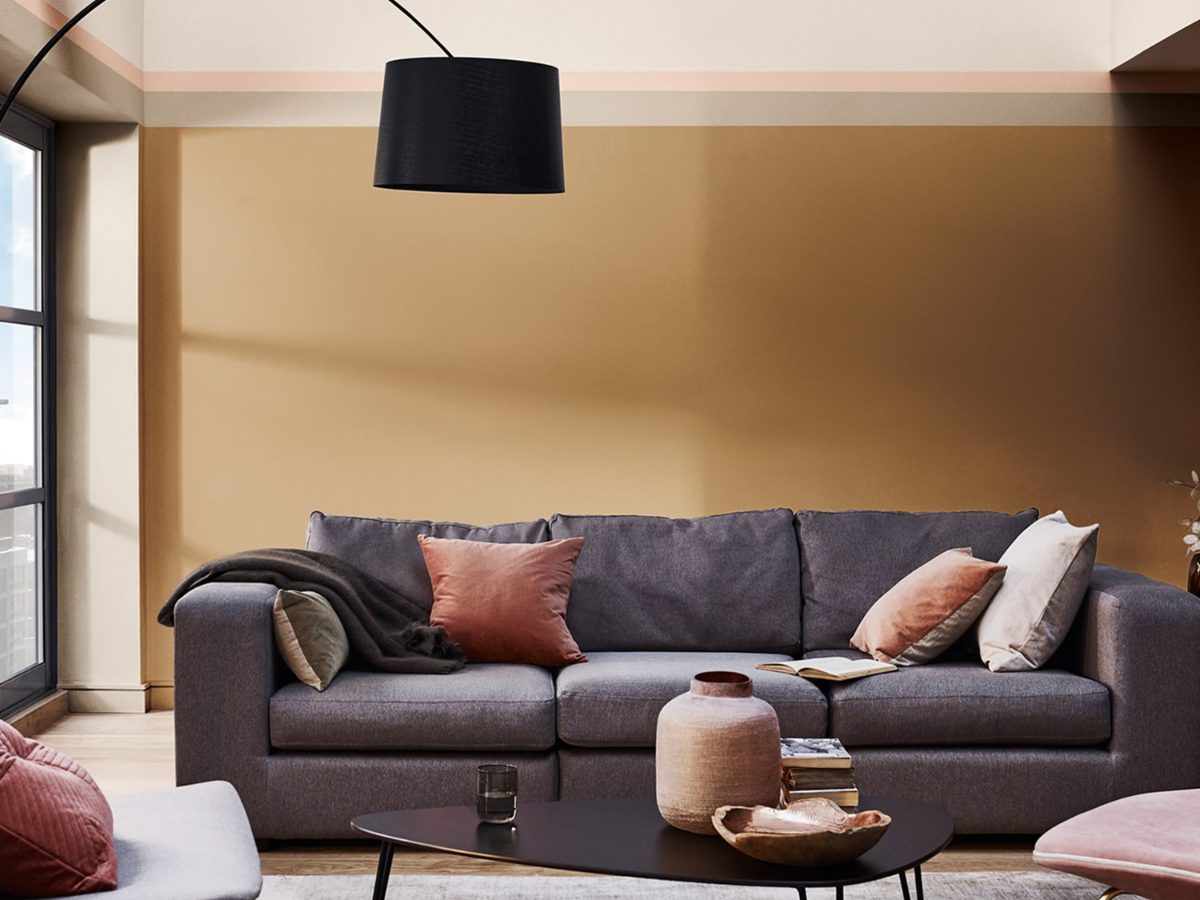 Soggiorno con parete color miele ambrato, divano grigio e cuscini terracotta