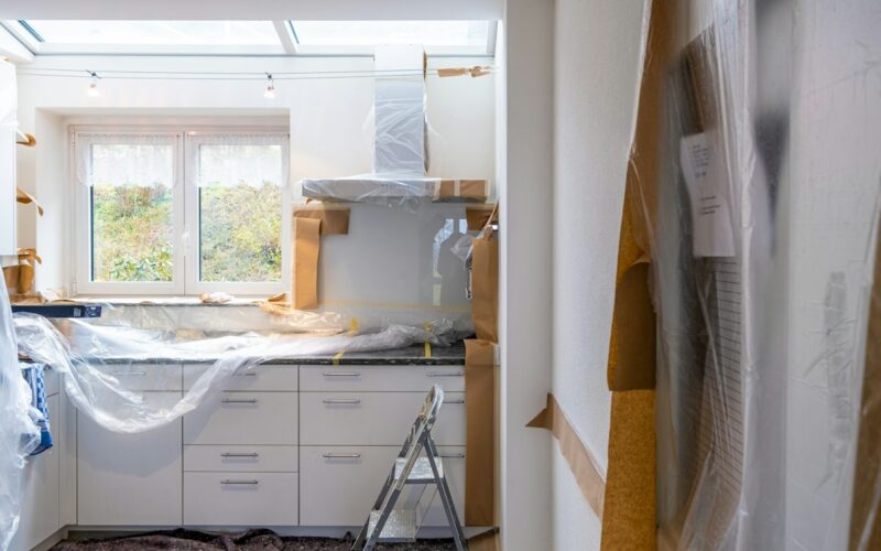 Cucina in ristrutturazione con mobili bianchi coperti da teli e attrezzi da lavoro