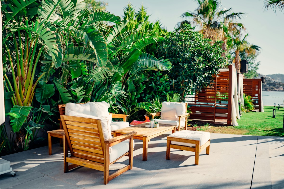Tavolo e sedie da esterno in legno chiaro in un giardino con piante tropicali