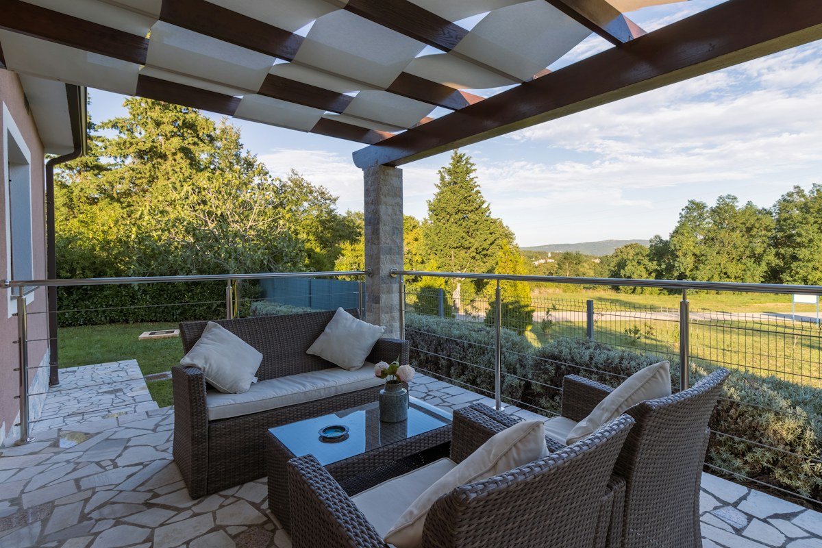 Poltrone e tavolino in rattan sintetico sotto una pergola con vista sul prato