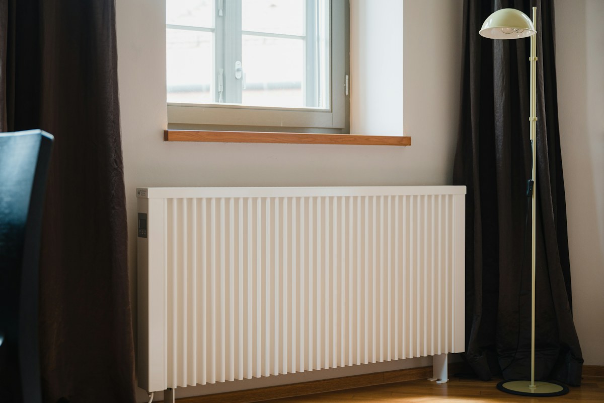 Termosifone bianco sotto una finestra in una stanza con pavimento in legno