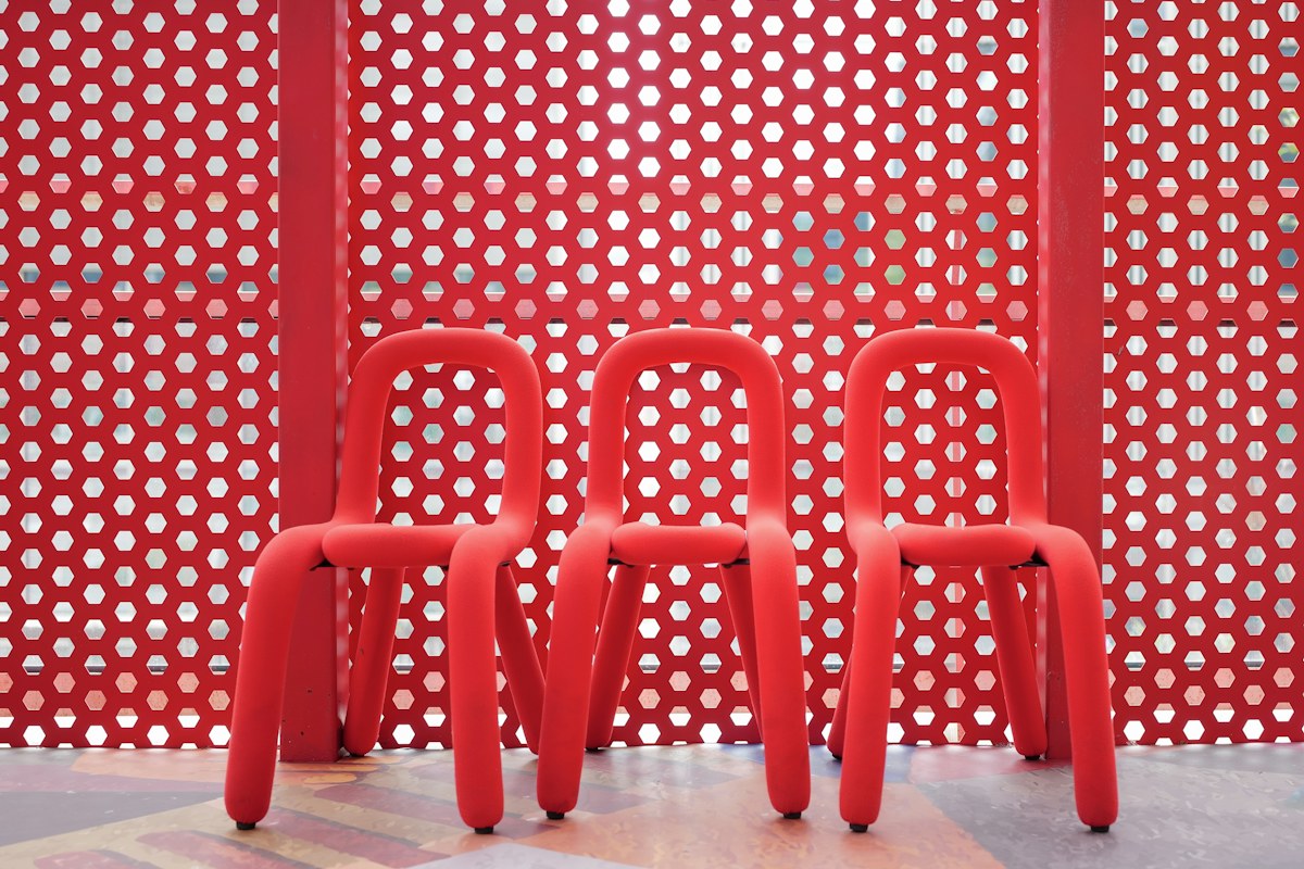 Tre sedie rosse in plastica davanti a una parete rossa traforata