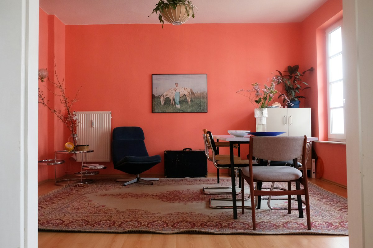 Soggiorno con pareti rosso corallo, tavolo in legno, sedie scure e tappeto