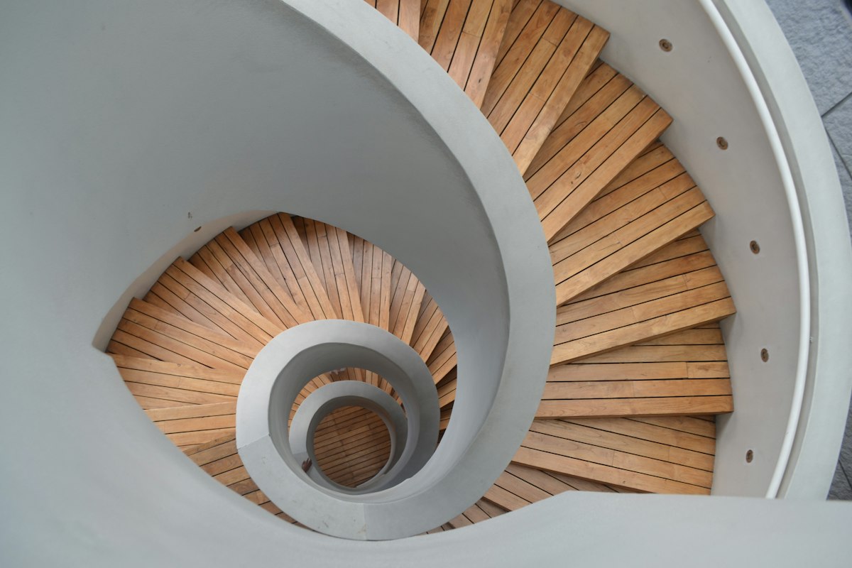 Scala a chiocciola con gradini in legno vista dall'alto accanto a una parete bianca