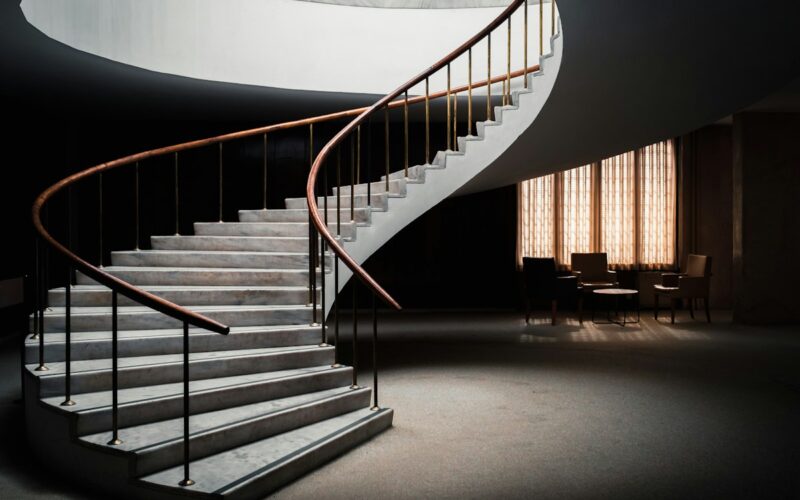 Scala curva con gradini chiari e ringhiera in metallo scuro in un interno