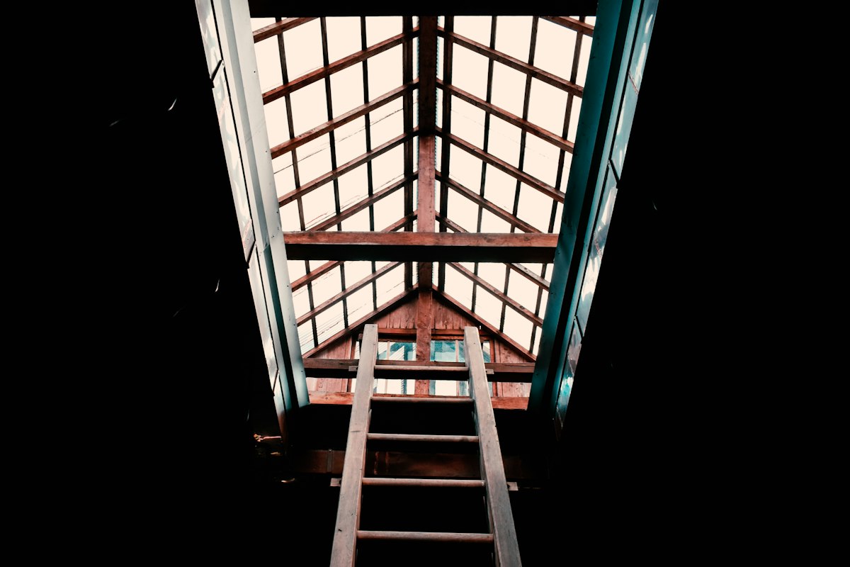 Scala a pioli in legno che sale verso un lucernario nel sottotetto