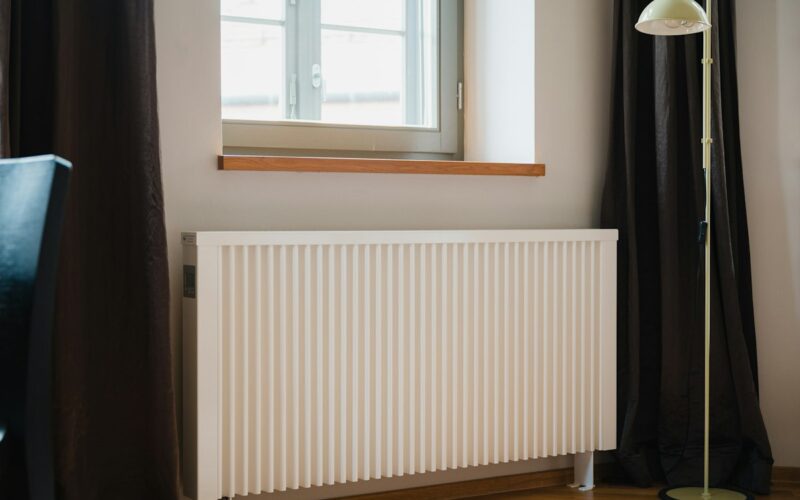 Termosifone bianco a piastra sotto una finestra in una stanza con tende scure